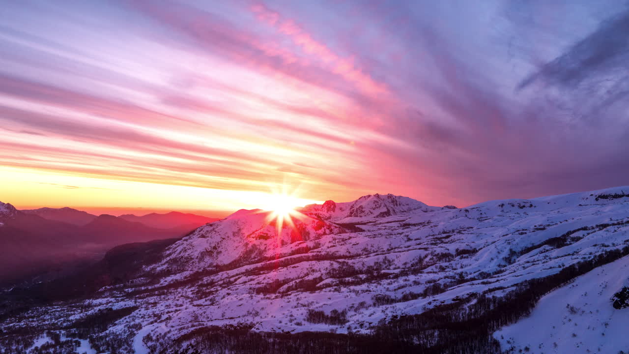 Aerial hyperlapse capturing a stunning sunset over the snowy Andes mountains in Chile, with dramatic skies and vibrant colors