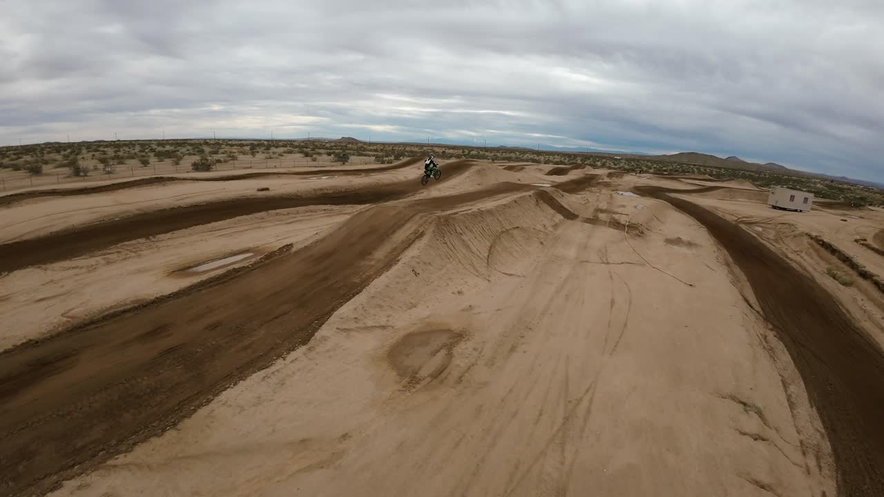 un motociclista vuela sobre un salto en una pista de carreras en el desierto de mojave en una emocionante muestra de habilidad - vista aérea en cámara lenta