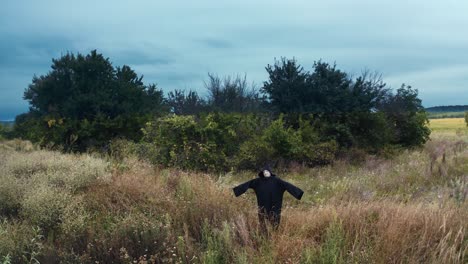 dark ghost with outstretched arms. scary figure of death in black mantle with hood standing on the field. motion camera back. halloween concept.