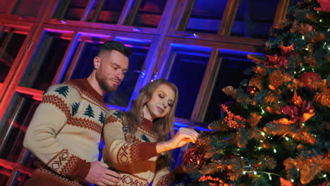 young family decorates christmas tree. cheerful girl is hanging christmas ball. couple in love prepare house for new year holidays. view from below.