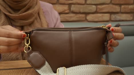 woman opens her brown handbag