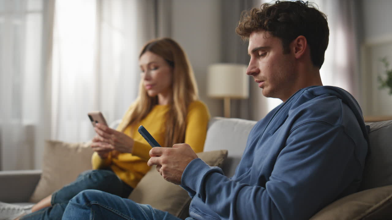 Online spouses using cellphones at cozy couch closeup. Serious woman looking man