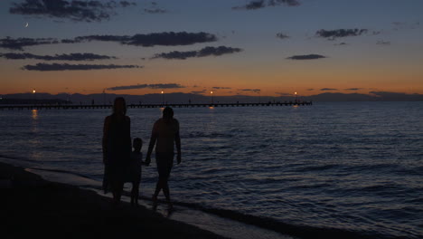 parents and child walking by the sea in dusk