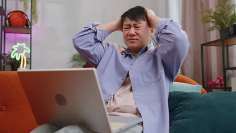 Asian-middle-aged-man-use-laptop-surprised-by-bad-news,-fortune-loss,-fail,-lottery-results-at-home