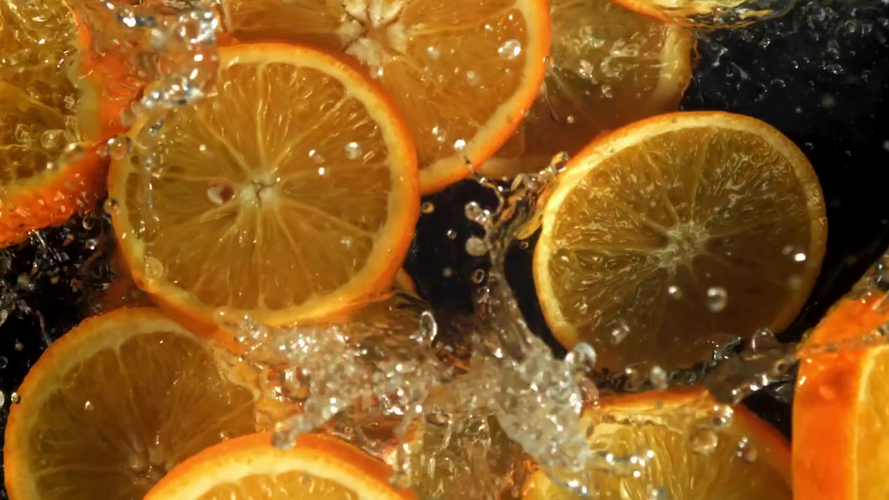 Orangenscheiben spritzen ins Wasser auf schwarzem Hintergrund