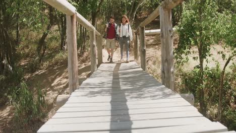 happy african american couple wearing backpack, hiking on boardwalk in forest, slow motion