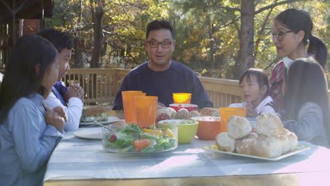 asian family at a table on a deck say a prayer before eating, shot on r3d