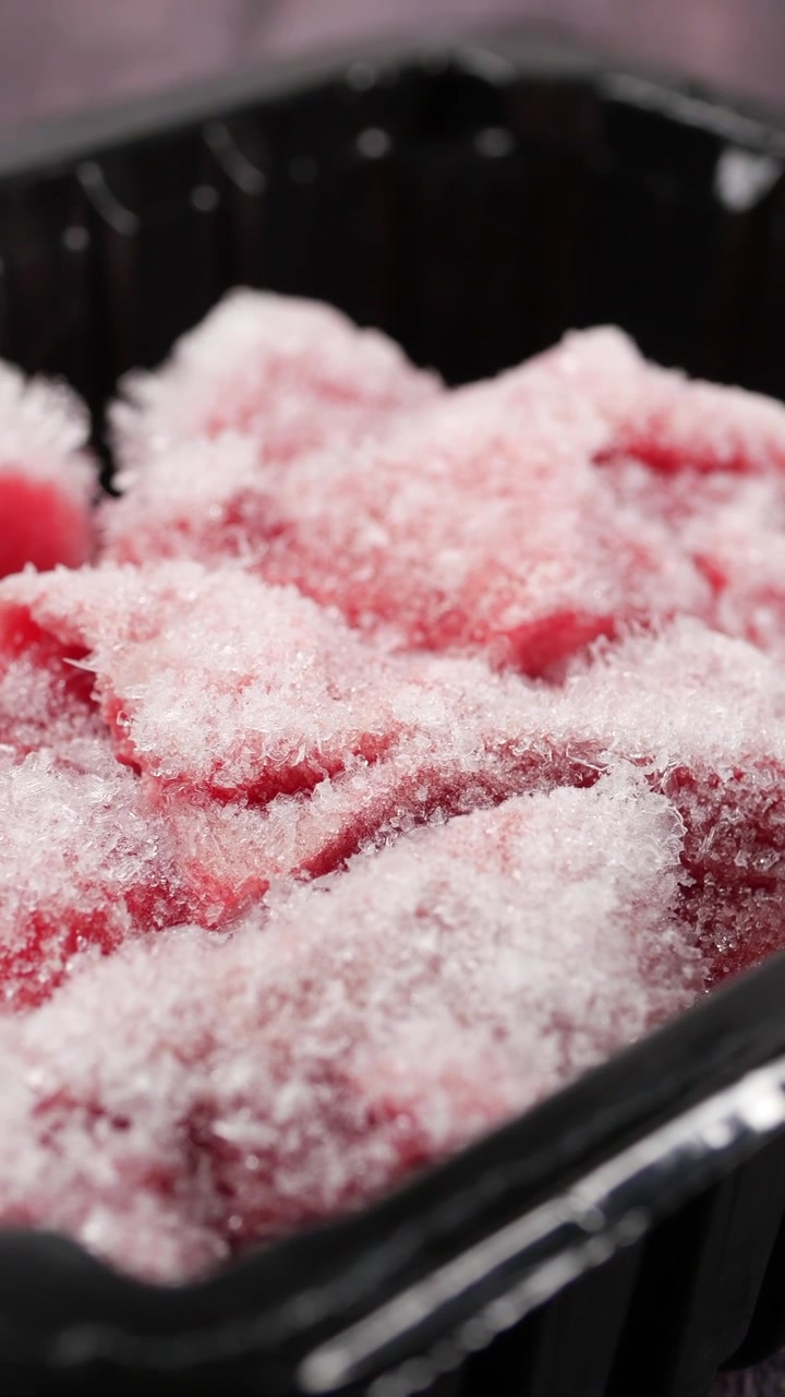 Primo piano di fette di carne cruda surgelata in un vassoio nero