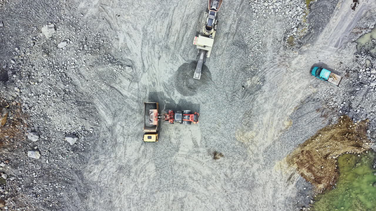 Granite quarry operation showing heavy machinery in action with trucks and a conveyor belt transporting stone materials