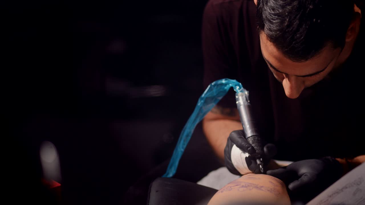 Hipster tattoo artist tattooing design with ink in professional studio