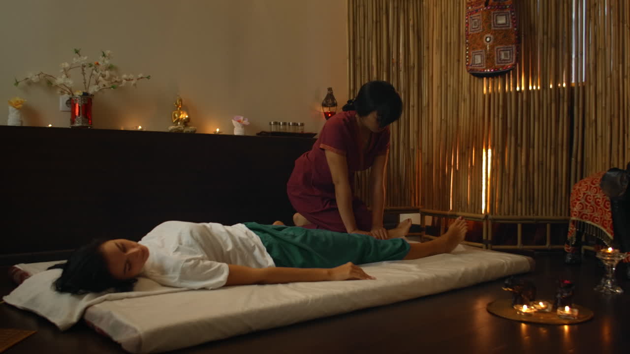 a Caucasian woman relaxes with a Thai massage at the Spa. Asian woman in traditional died performs massage on the back.