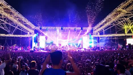 una gran multitud en un concierto con un escenario iluminado y confeti cayendo del cielo