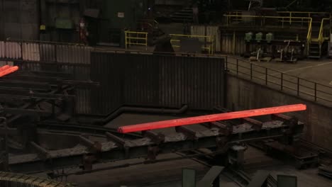 glowing steel bars on a conveyor in a dimly lit industrial steel mill, evoking a sense of heavy industry at work