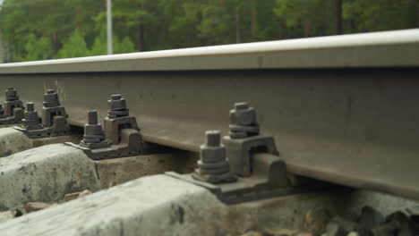 close-up view of railway track fastenings with bolts and nuts securing rails to concrete sleepers with a view of gravel and vegetation in the background