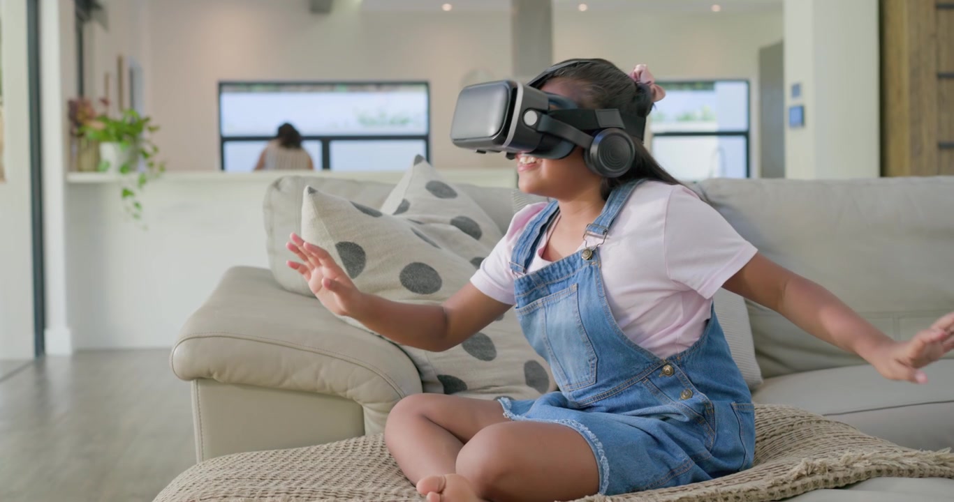 Ragazza afroamericana che indossa cuffie per visore VR, che fa gesti VR interattivi su un divano beige