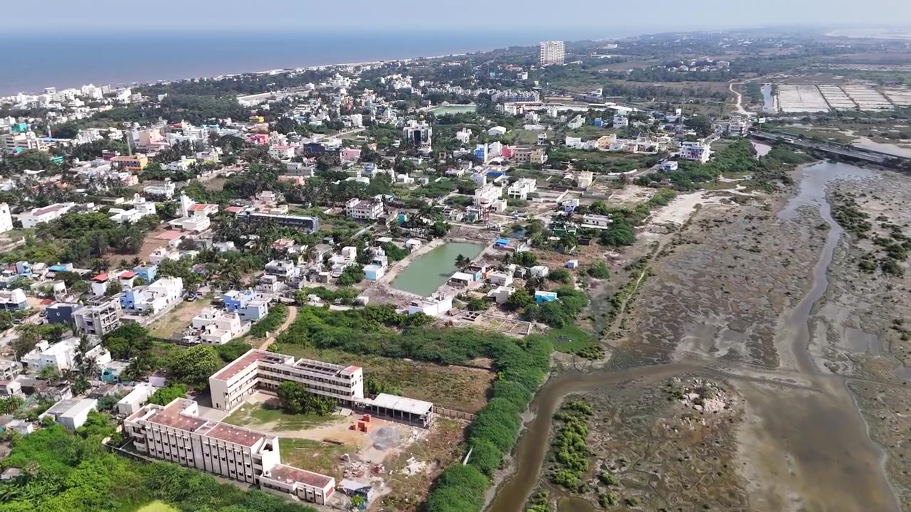 Vista aerea cinematografica dell'estuario di Kovalam che mostra distese di fango tidali esposte, corsi d'acqua tortuosi, mangrovie lussureggianti, quartieri residenziali e la costa del Golfo del Bengala.