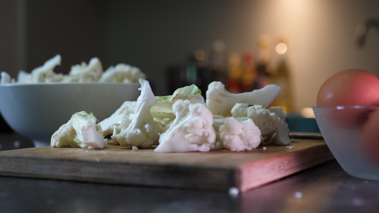Close-up shot of chopped cauliflower on a wooden cutting board in dim kitchen lighting, with soft focus on ingredients creating a cozy and fresh cooking atmosphere