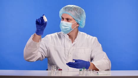 profesional de la salud con un traje de protección, máscara y guantes examina muestras de vacuna en viales. concepto de investigación de fármacos para el coronavirus covid-19. clave de croma de pantalla azul. primer plano. cámara lenta