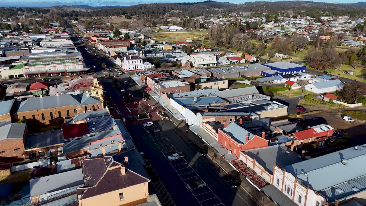 Drone footage captures a sunny daytime aerial view of a busy city junction with commercial buildings and light vehicle traffic in Glen Innes, Australia