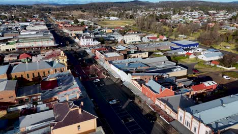 drone footage captures a sunny daytime aerial view of a busy city junction with commercial buildings and light vehicle traffic in glen innes, australia