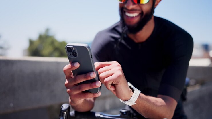 Glücklicher Radfahrer nutzt Smartphone im Freien an einem sonnigen Tag