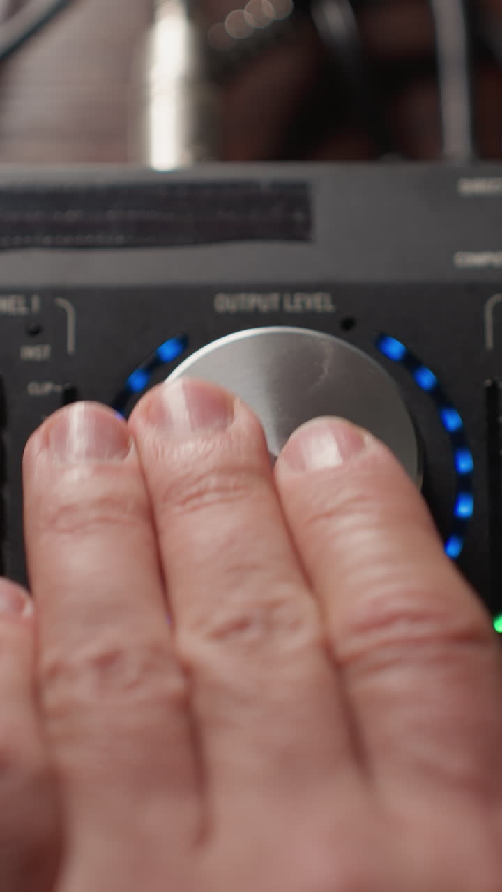 primer plano de una mano que opera un mezclador de sonido, girando una perilla grande hacia la izquierda para ajustar los niveles de audio. con la interfaz iluminada del mezcladora y varios controles visibles