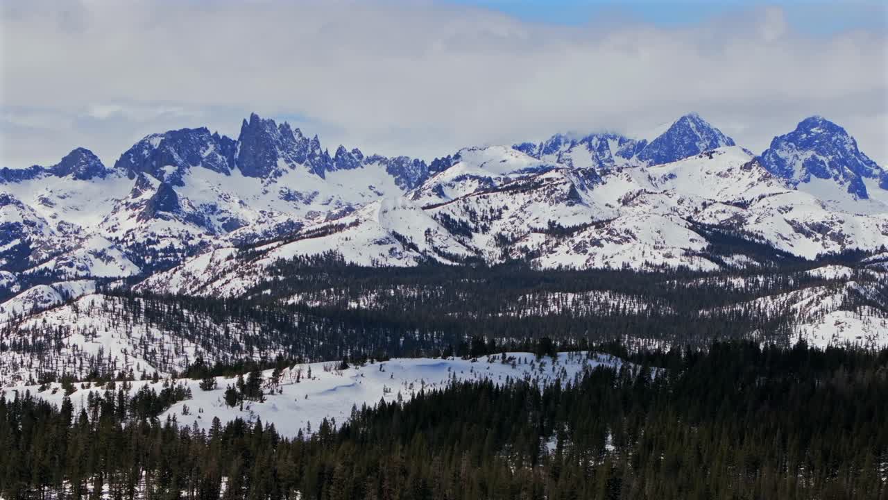 Banner peak Volcanic ridge Minaret Summit Pass Mammoth Mountains vista Parallax winter aerial drone California group jagged towering snow covered peaks sunny blue sky Inyo forest Sierras PCT upwards