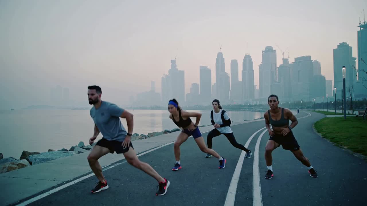 Leader maschile che avvia i passi, con donne che mimano gli affondi laterali, riscaldandosi per il fitness in riva al mare.
