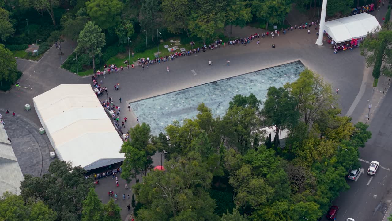 Aerial shot showing lines of people around water feature in CDMX park