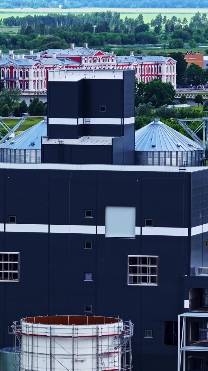 Vista aérea cercana de un edificio industrial y estructuras de almacenamiento dentro de un complejo de producción, dron asciende para revelar una oficina gubernamental histórica, vertical.