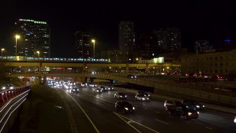 Cars-and-trucks-stuck-in-traffic-on-freeway-at-night-in-Chicago-as-trains-pass-over-the-highway-4k