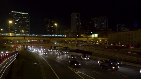 cars and trucks stuck in traffic on freeway at night in chicago as trains pass over the highway 4k