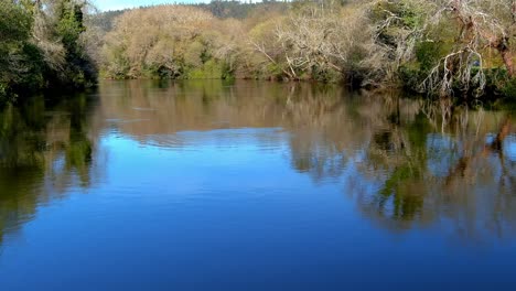 Drone-Flying-Backwards-Over-Calm-Reflective-Waters-Of-River-Tambre