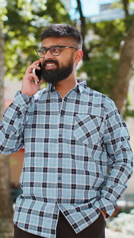 Happy-Indian-man-having-remote-conversation-talking-on-smartphone,-good-news-gossip-in-city-street