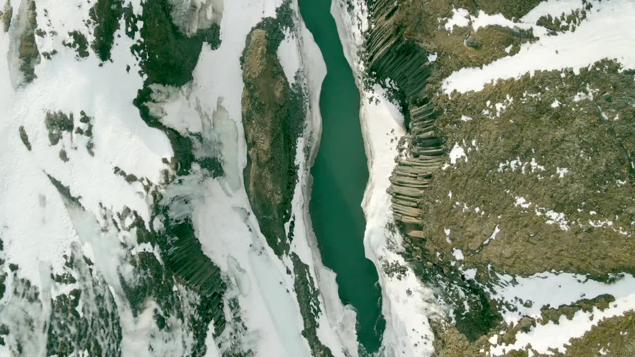 Aerial, drone-captured footage offers a distinctive perspective of azure water meandering through rocky glaciers nestled amidst the mountains