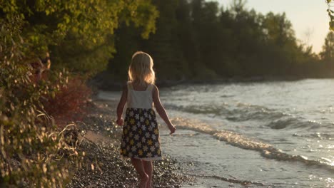 Junges-Blondes-Mädchen,-Das-Bei-Sonnenuntergang-Am-Kiesstrand-Entlang-Geht