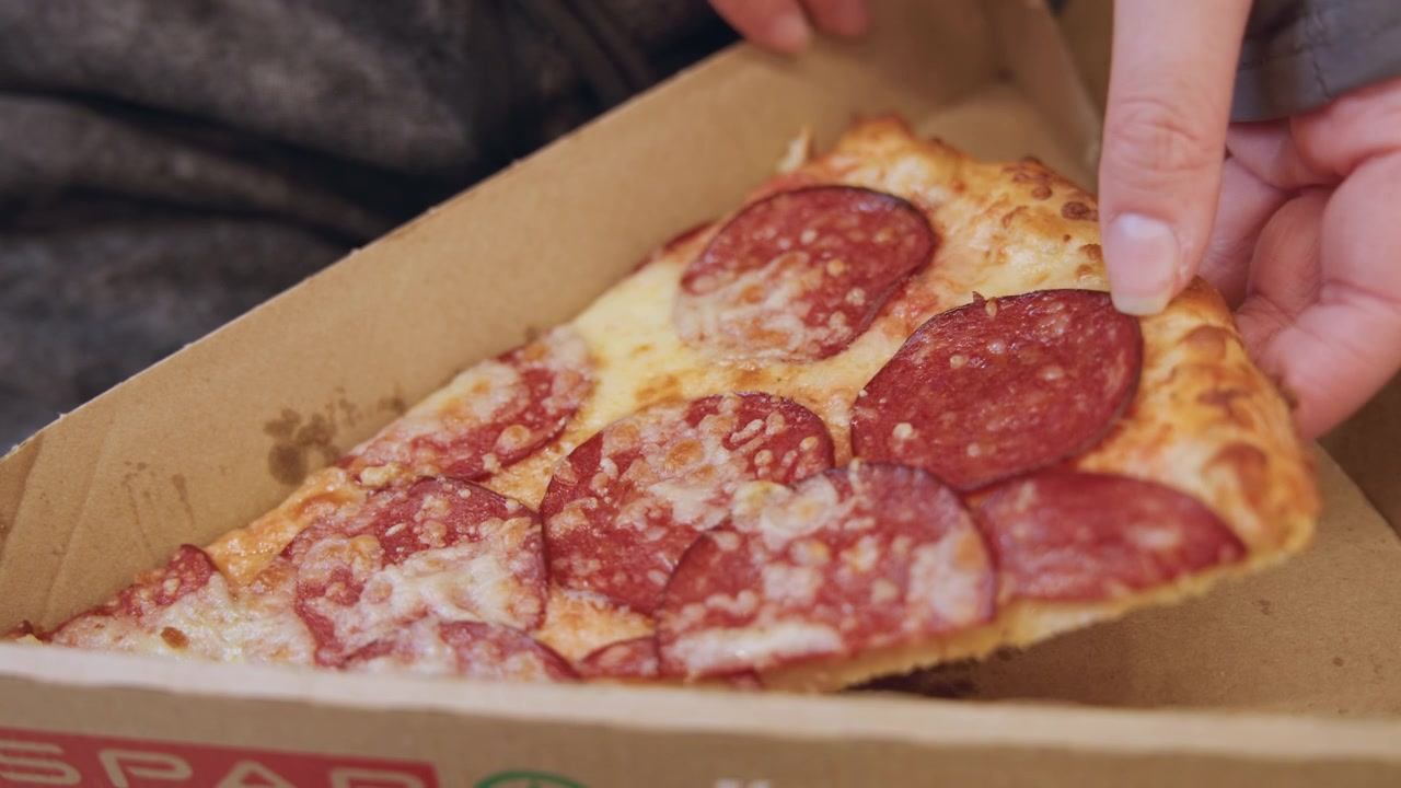 Kutudan pepperoni pizza dilimi alan el, yağlı kartonun ve boş köşelerin yakın çekimi, gece atıştırmalıkları için sıradan bir paket servis sahnesi, sıcak erimiş peynir ve çıtır kabuk, gayri resmi rahatlatıcı yemek