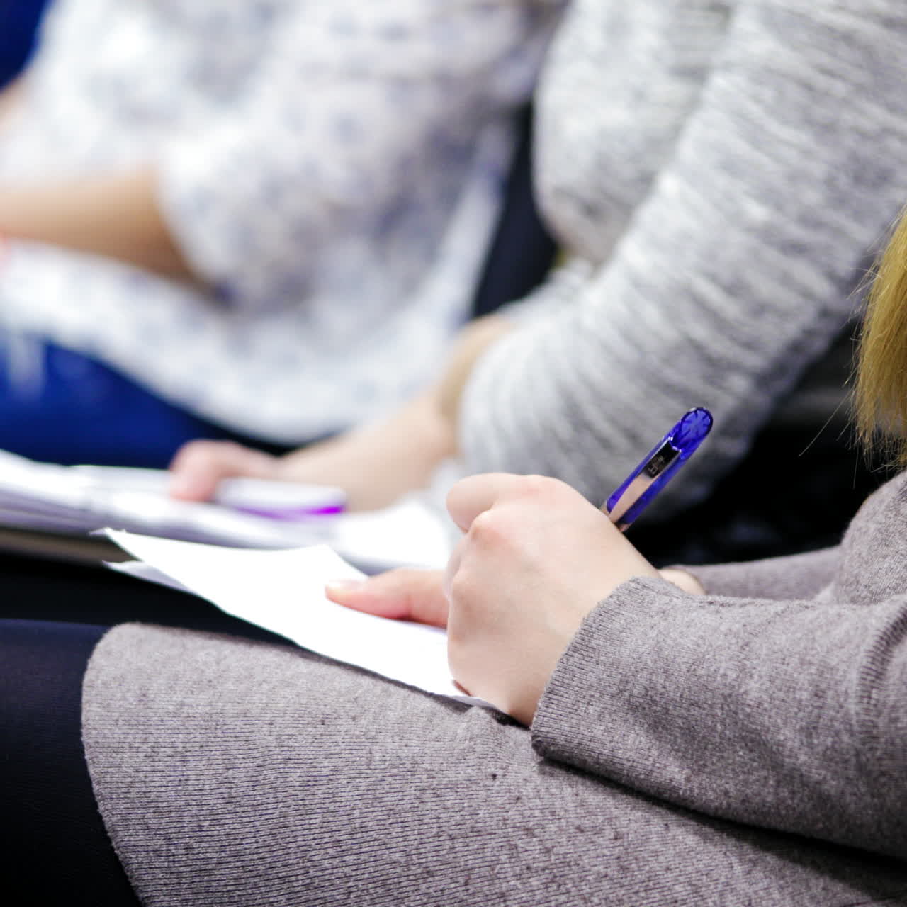 Young employees are writing, sitting at working conference indoors. Women are taking notes on sheets at business meeting.