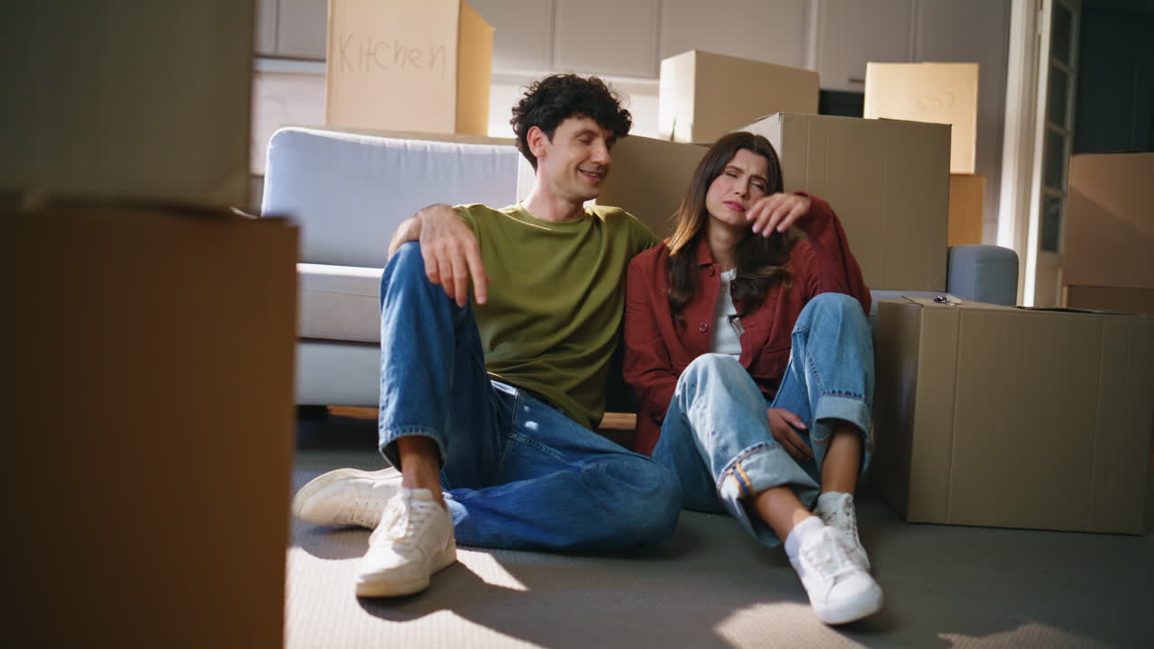 Tired couple moving mortgage talking around cardboard boxes. Family rest floor