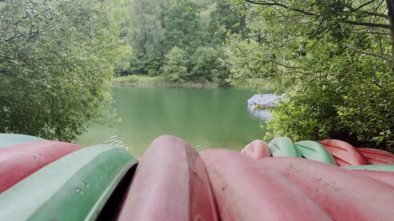 Red canoes lie lined up on the banks of a small lake in nature and wait for new guests