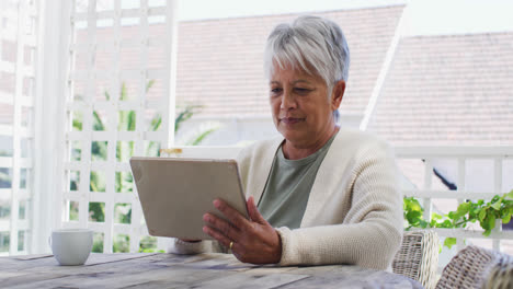 Ältere-Frau-Mit-Gemischter-Abstammung-Trinkt-Kaffee-Mit-Tablet-Im-Garten