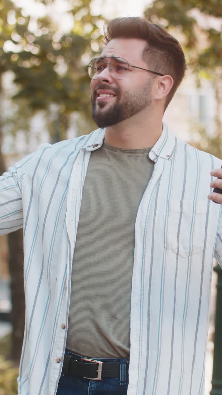 Upset young man using smartphone typing browsing loses becoming shocked bad news on city street