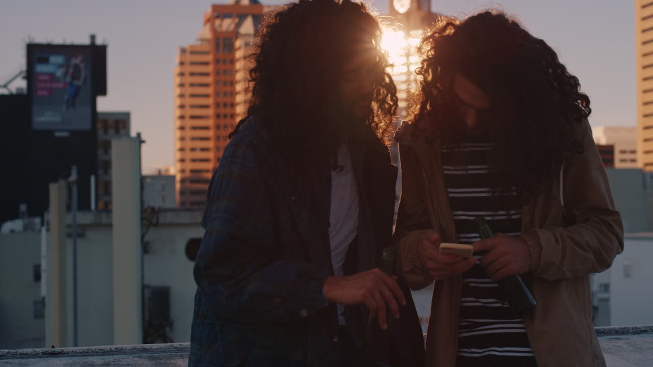 freunde, die smartphone-mobiltechnologie benutzen, die bei sonnenuntergang auf dem dach rumhängen, das wochenende genießen, chatten, social-media-nachrichten im städtischen hintergrund teilen