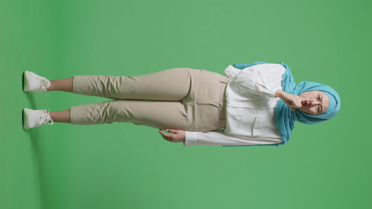 녹색 스크린 배경 스튜디오에 서있는 동안 카메라를보고 shh 제스처를하는 아시아 무슬림 여성의 몸이 가득 차 있습니다.