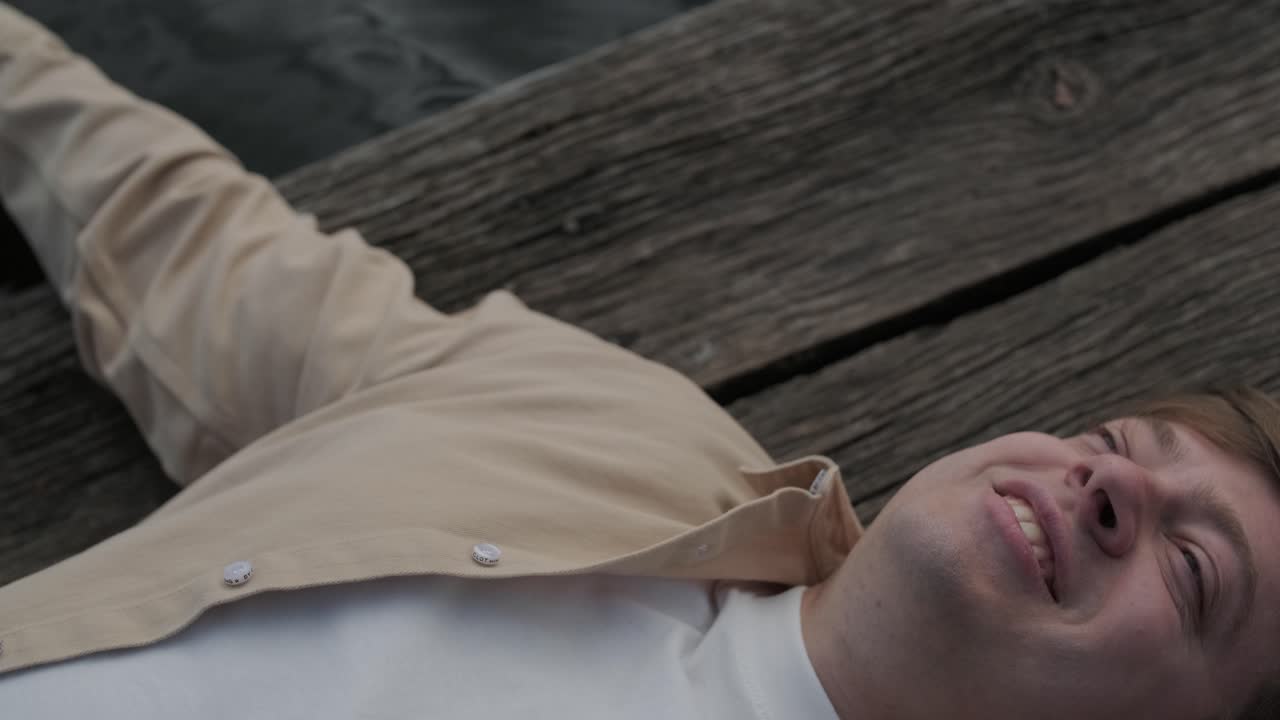 젊은이가 나무로 된 보행자 다리 위에 혼자 누워서 호수를 쳐다보고, 삶에 대해 생각하고, 자연에서 평화로운 분위기를 누리고, 신선한 공기를 즐기고, 뒤를 바라보고 있습니다.