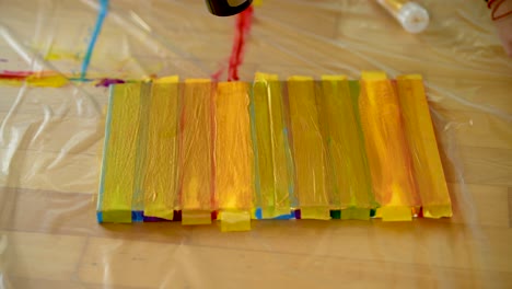 una mujer que usa cinta de pintores para terminar sus rayas de colores en un lienzo