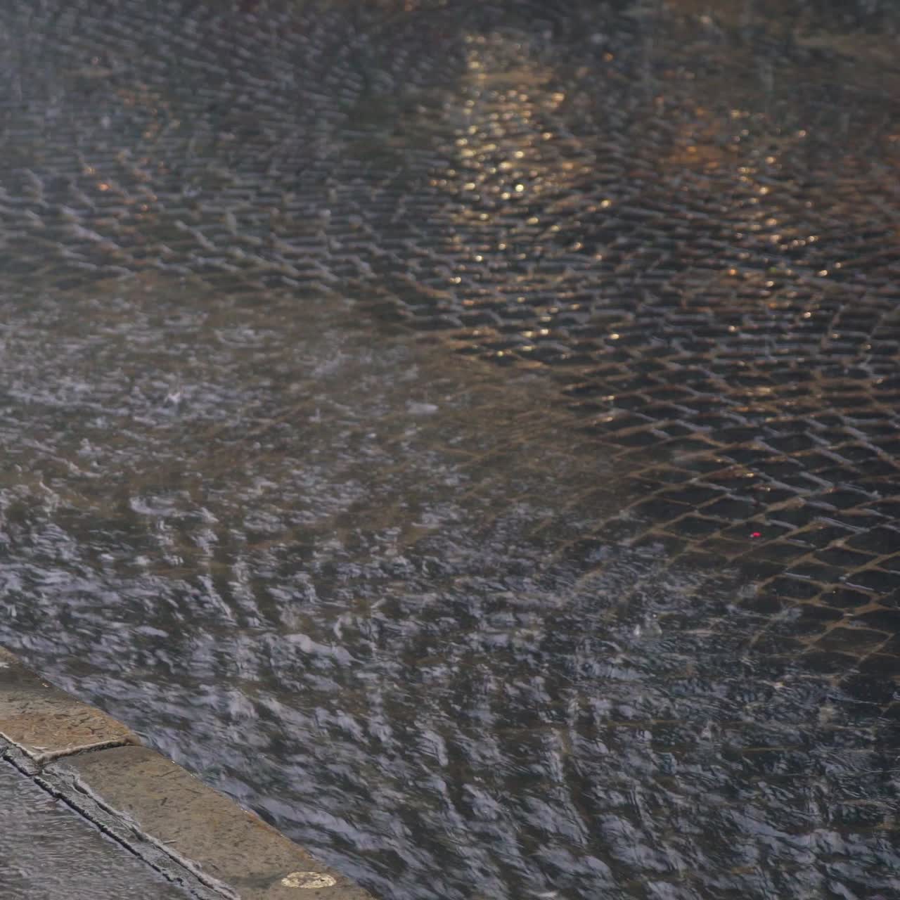 rain drops are turning into a stream of water which flowing on the pavement. It's raining in the city