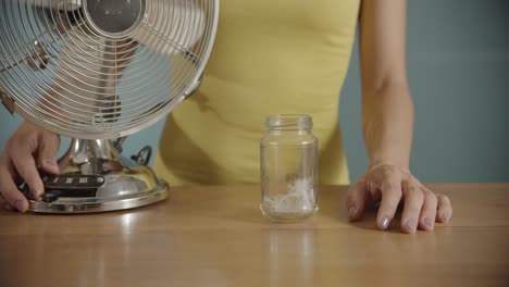 Close-up-shot-of-woman's-hands-turning-on-an-electric-fan-and-blowing-feathers-on-air