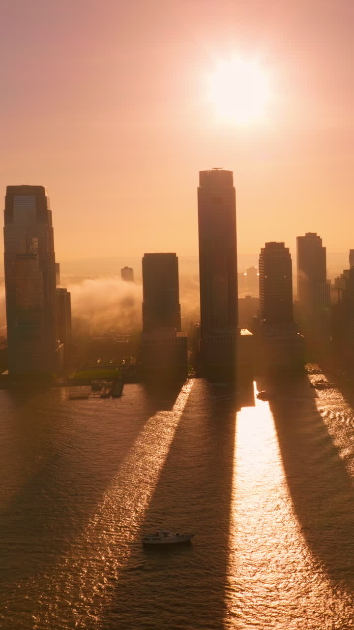 Manhattan Island at setting sun and thickening fog. Skyscrapers throwing long shadows on the water. Beautiful pink sky backdrop. Vertical video