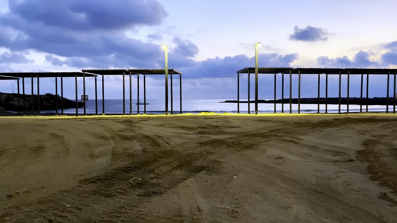 спокойный вечер разворачивается в прибрежном доке, когда золотые огни мерцают на песчаной тропе, ведущей к спокойному морю. облака мягко дрейфуют в сумеречном небе.